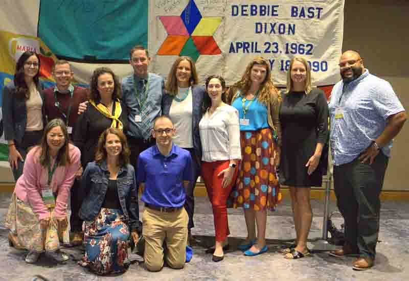 Several people behind a mural that says "Debbie Bast Dixon." They all have their hands on each other's shoulders, posing for a photo.